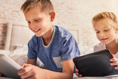 παιδιά ξαπλωμένα στο κρεββάτι παίζουν στα tablet τους