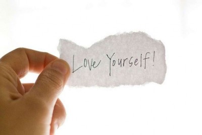 που κρατάει ένα χαρτί που γράφει love yourself