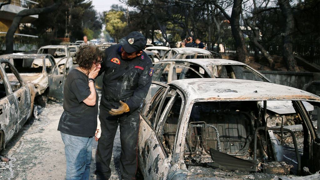 ψυχολογικά φορτισμένη γυναίκα που κλαίει στον ώμο ενός πυροσβέστη κοιτάζοντας το καμένο αμάξι της μετά καταστροφικό γεγονός